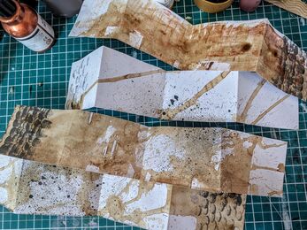 Four strips of rectangular paper painted with browns and blacks on an artist's table