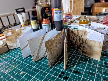 A folded booklet in a concertina shape covered in brown and black marks