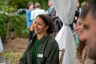 A woman smiles at an outdoor event seated beside other smiling people