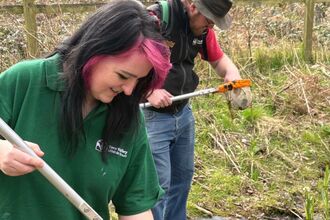Two people look into pond dipping nets beside a pond