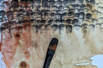 A paintbrush lays beneath a series of black marks made in the shape of feathers