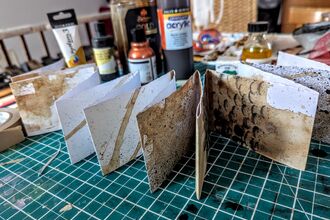 A folded booklet in a concertina shape covered in brown and black marks