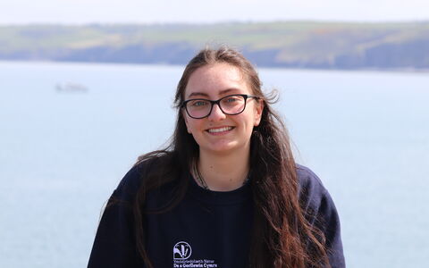 Maddy smiling at the camera, with the sea behind her