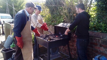 Three people around an outside forge