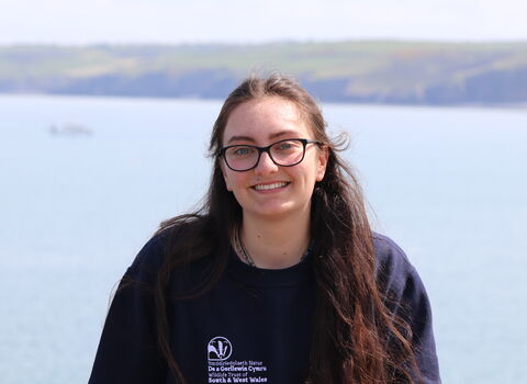 Maddy smiling at the camera, with the sea behind her