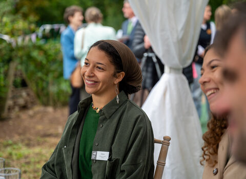 A woman smiles at an outdoor event seated beside other smiling people