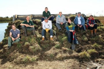 Volunteer group sitting for a photo on top of an artificial sand martin bank they are creating.