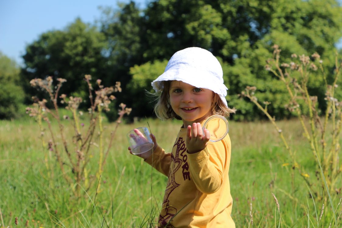 Young girl on a nature reserve looking for mini-beasts with her bug pot and magnifier. 